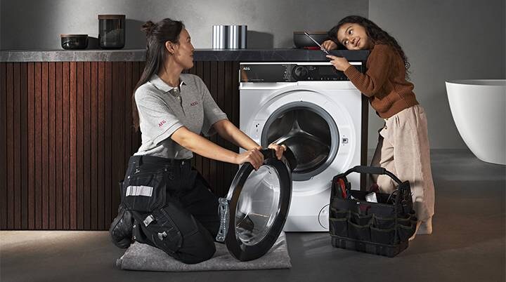 Mulher a substituir a porta da máquina de lavar enquanto uma jovem assiste