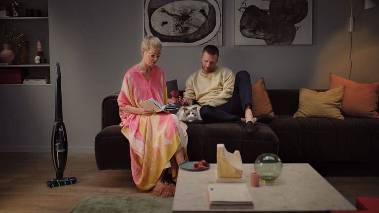Casal numa sala de estar com um aspirador sem fio no fundo