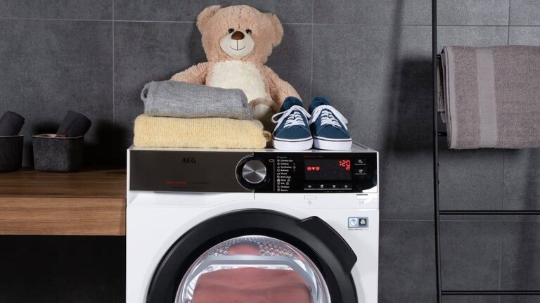 Urso de peluche ao lado de roupas e sapatos em cima de uma máquina de lavar AEG.